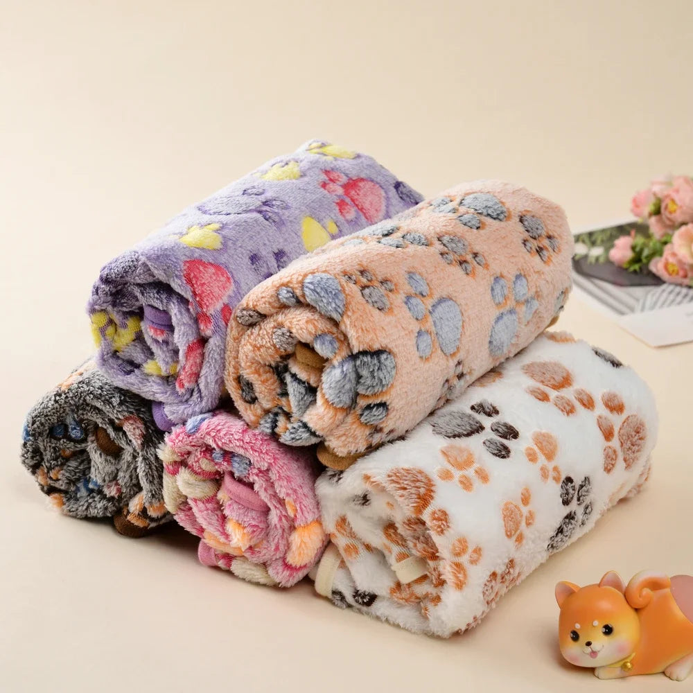 A stack of cozy thick fleece pet blankets featuring various pastel and earthy tones with paw print patterns.