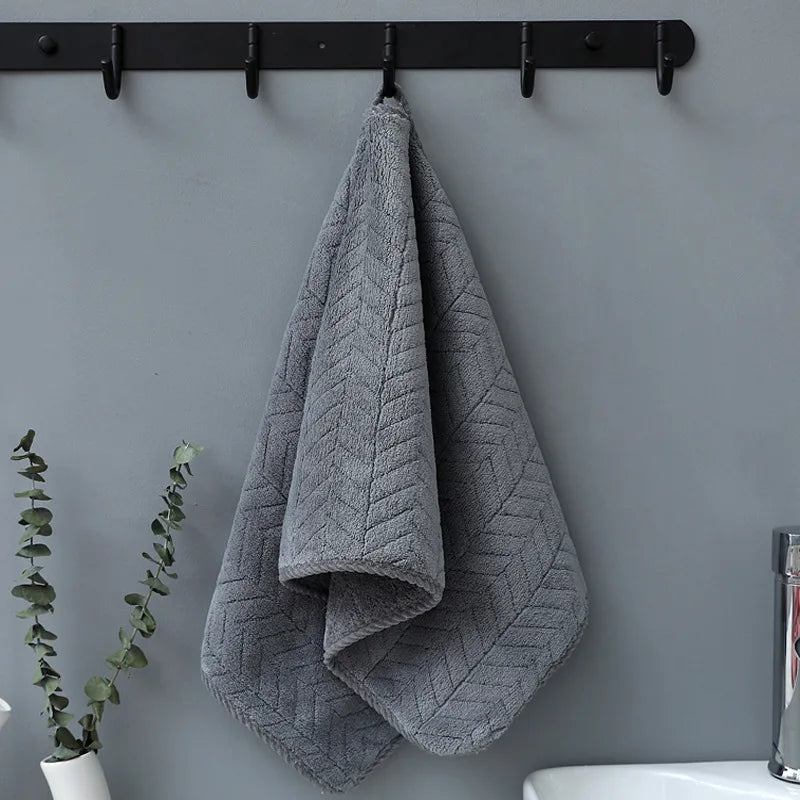 A gray plush microfiber bath towel is hanging on a black rack against a gray wall.