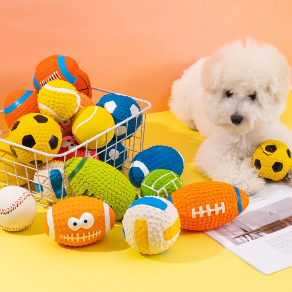 A white poodle sits next to a collection of colorful squeaky latex balls for dogs on a yellow surface.