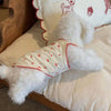 A white pet tank top with a cherry print design and red stitching is displayed on a light-colored fabric.