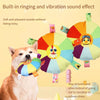 A dog is playing with a colorful plush flying disc toy that makes ringing and vibration sounds.