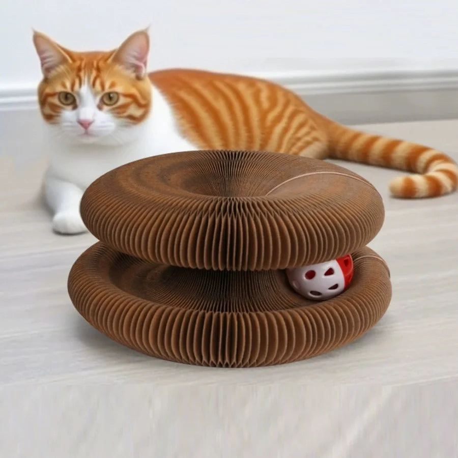A fluffy orange and white cat is sitting next to two brown, circular foldable cat scratcher boards with a ball and bell track