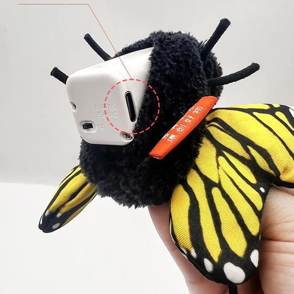 A black fuzzy cat toy with yellow butterfly wings and a white electronic device attached.