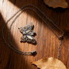 Silver butterfly ashes pendant necklace resting on a dark wooden surface with dried leaves.