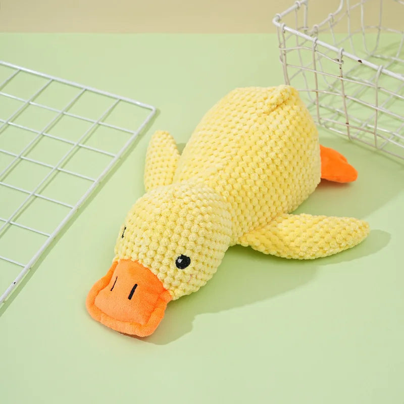 A yellow knitted plush duck toy lying on a light green surface next to a wire mesh basket.