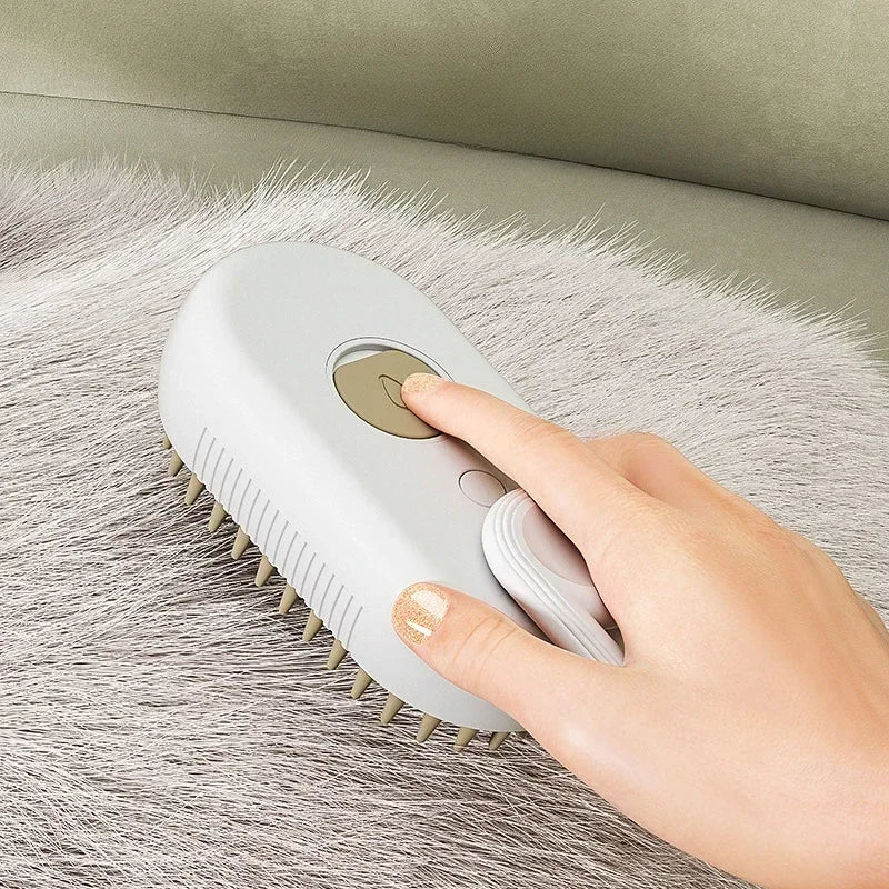 A hand is operating a white pet grooming brush with a steam spray on a fluffy gray surface.
