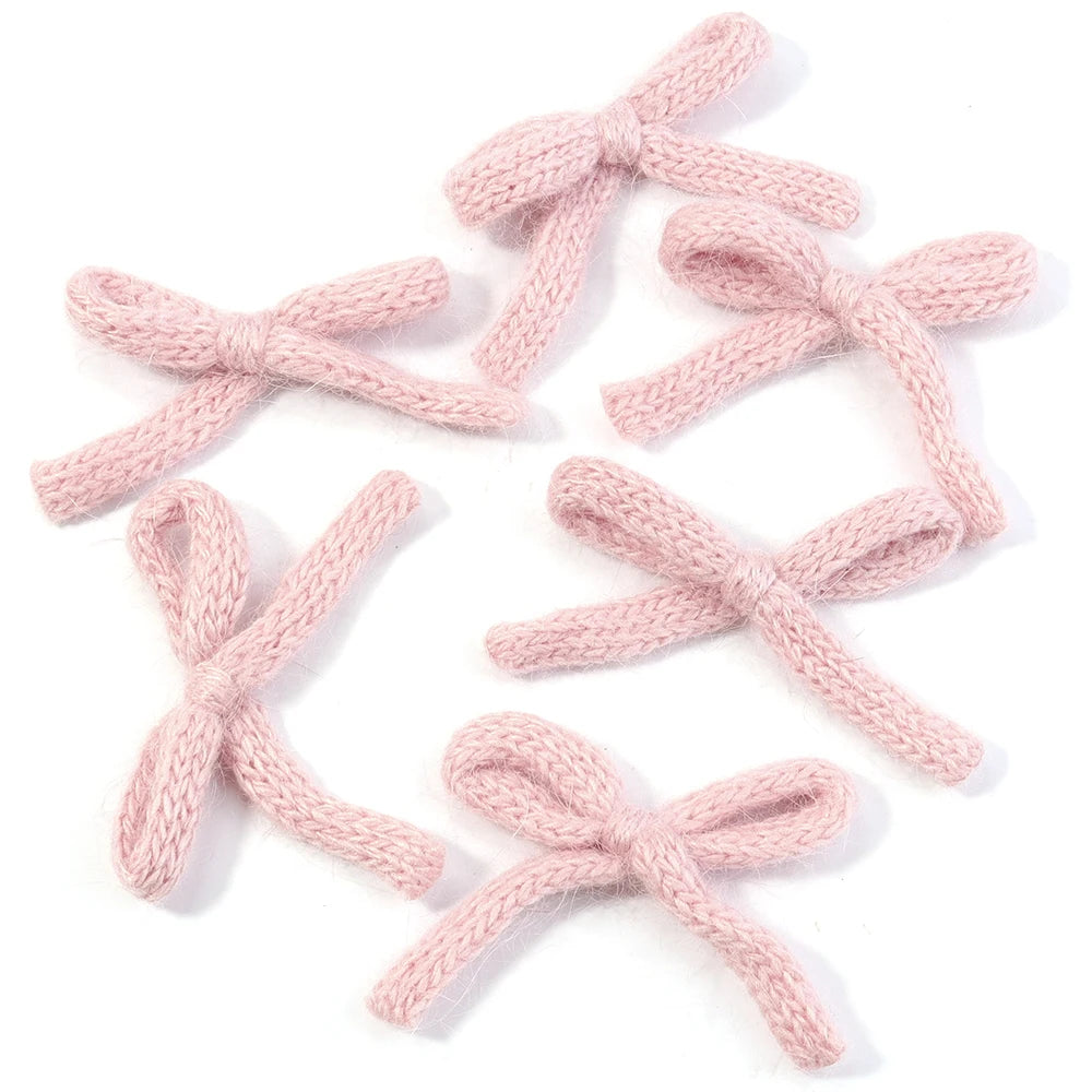 A set of six handmade knitted cotton bows in a pale pink color.