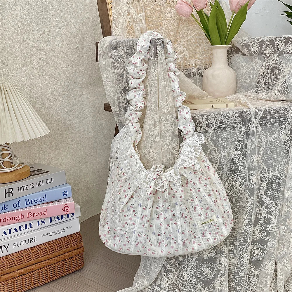 A white floral lace bowknot shoulder bag with a pleated design resting on a lace tablecloth.