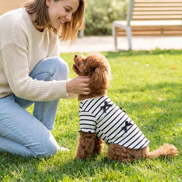 A woman is gently petting a fluffy brown dog wearing a black and white striped shirt in a grassy outdoor setting.