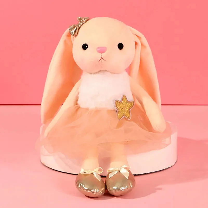 A soft peach colored plush rabbit toy with pink ears and a gold star decoration.