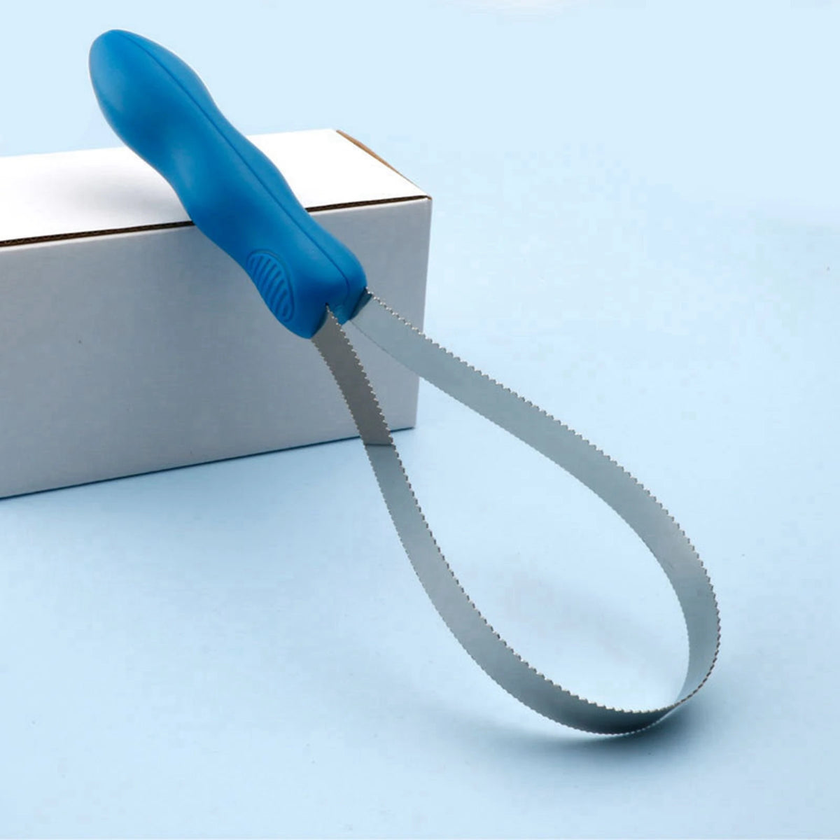 A blue expandable dual-sided grooming comb with silver blades rests on a white box.
