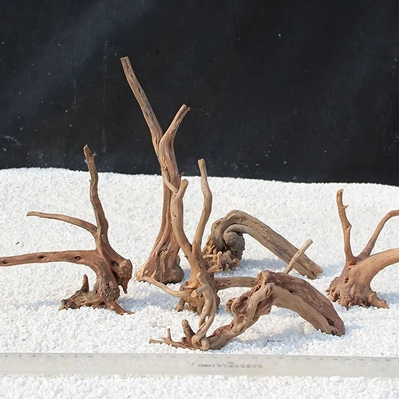 Driftwoodstücke aus Naturholz auf weißem Kies vor dunklem Hintergrund.