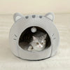 A gray plush tent house shaped like a cat's head with ears, containing a small tabby kitten.