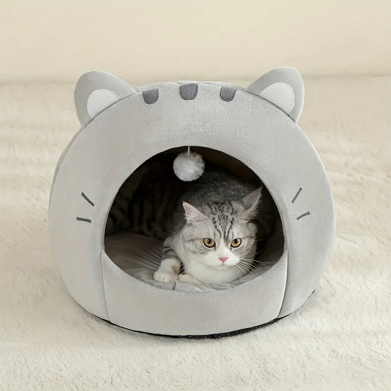 A gray plush tent house shaped like a cat's head with ears, containing a small tabby kitten.