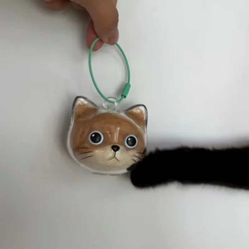 Kleines, hellbraunes Katzencharm mit großen Augen, an einem grünen Ring-Anhänger gehalten.