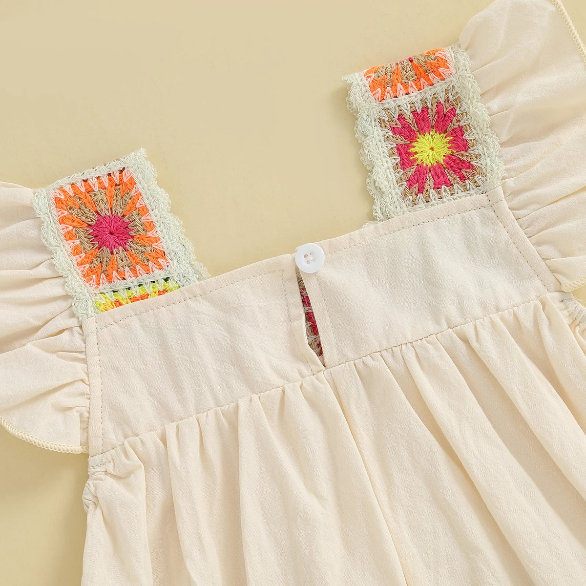 A light pink toddler romper featuring floral embroidery details on the chest and ruffled sleeves.