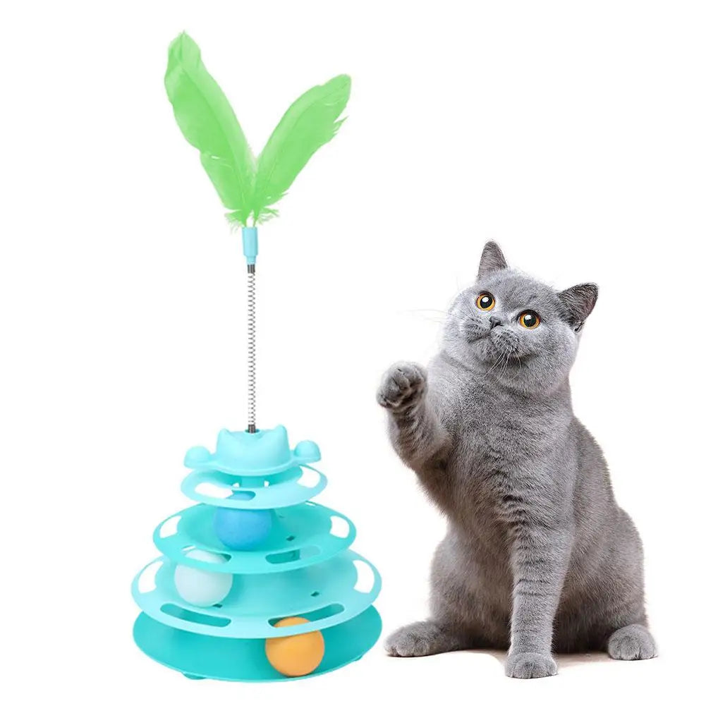 A gray cat is sitting next to an interactive rotating feather toy tower with green feathers and blue components.