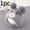 A knitted grey dog winter hat with fluffy bear ears resting on a gray fabric.