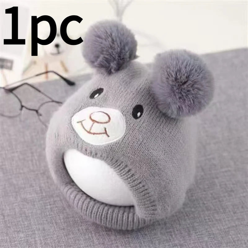 A knitted grey dog winter hat with fluffy bear ears resting on a gray fabric.