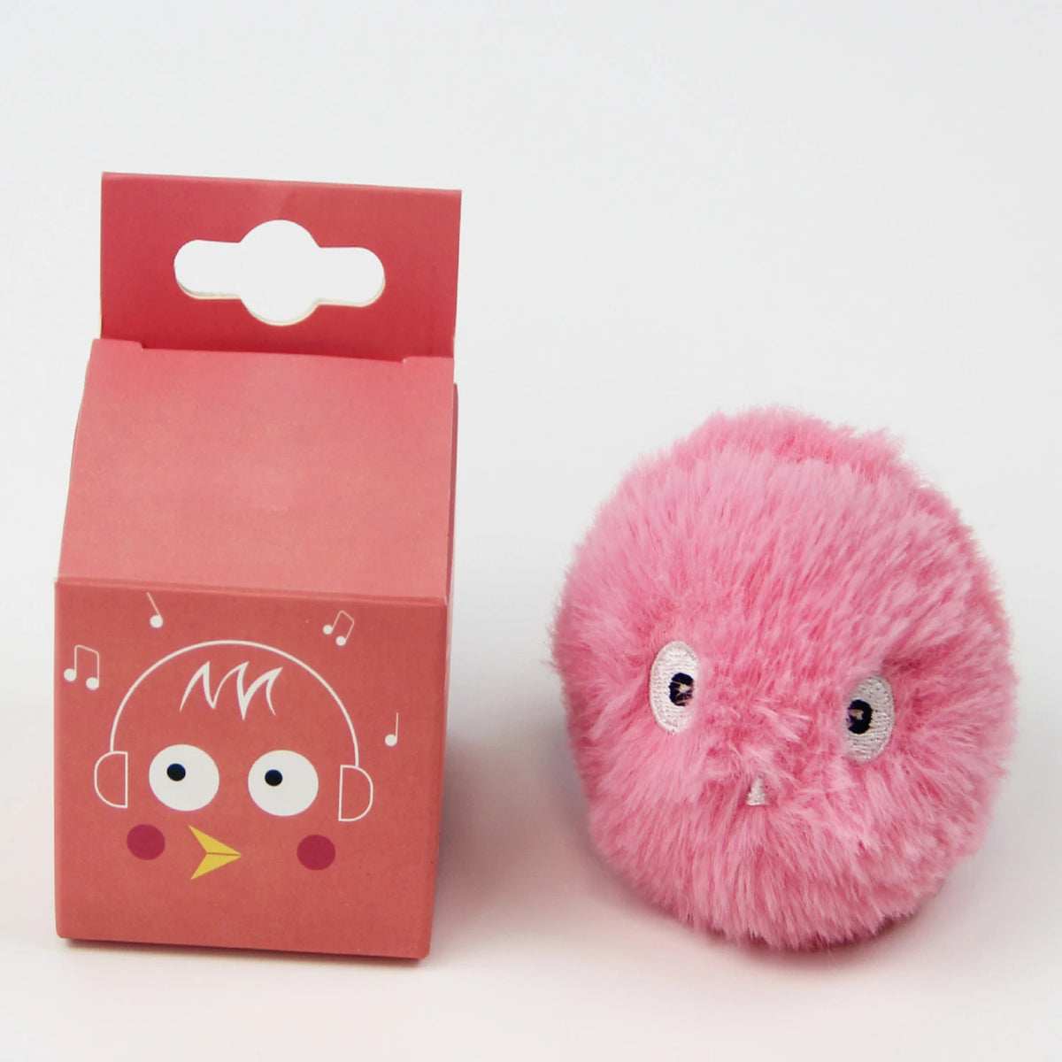 Jouet en peluche rose et moelleux en forme d'oiseau avec de grands yeux et des écouteurs, à côté de sa boîte.