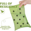 A hand is holding a light green biodegradable dog poop bag with black paw prints on it.
