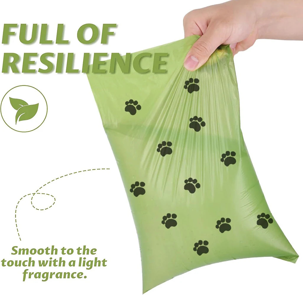 A hand is holding a light green biodegradable dog poop bag with black paw prints on it.