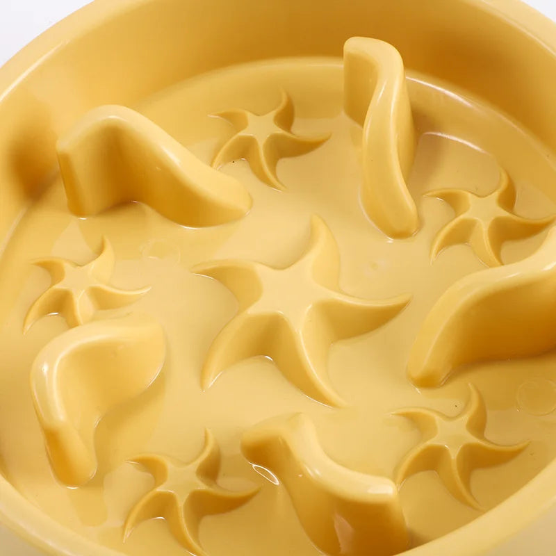 A yellow anti-slip slow feeder bowl filled with liquid, featuring molded star and curved shapes for pet feeding.