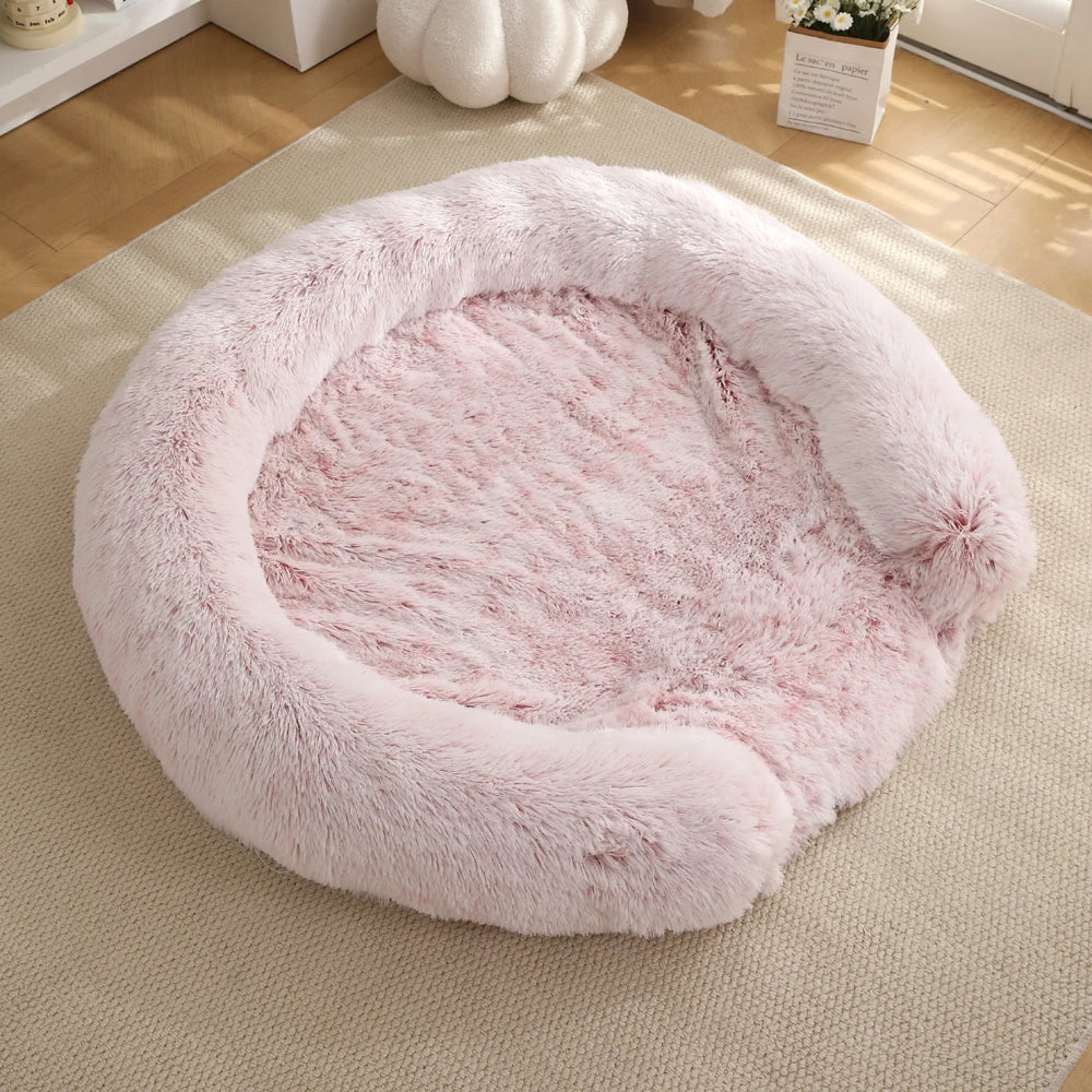 A round, fluffy pink dog bed with a removable cover resting on a light beige rug.