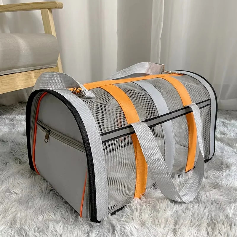 A gray and orange lightweight foldable mesh travel carrier bag for small pets resting on a white fluffy rug.