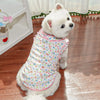 A white dog wearing a floral patterned vest with pink trim.