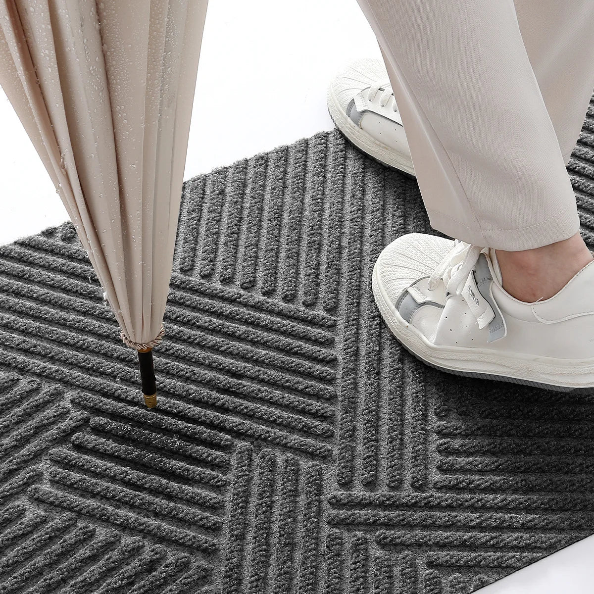 Close-up of a person's legs and feet wearing white shoes standing on a dark gray geometric non-slip doormat.