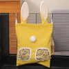 A yellow multi-hole hay feeder bag with white ears and a round white nose is displayed in a dark container.