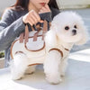 A fluffy white dog wearing a brown and white portable pet carrier sling bag, held by a person.