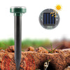 A black solar ultrasonic pest repeller device is shown inserted into soil, with a solar panel visible nearby.