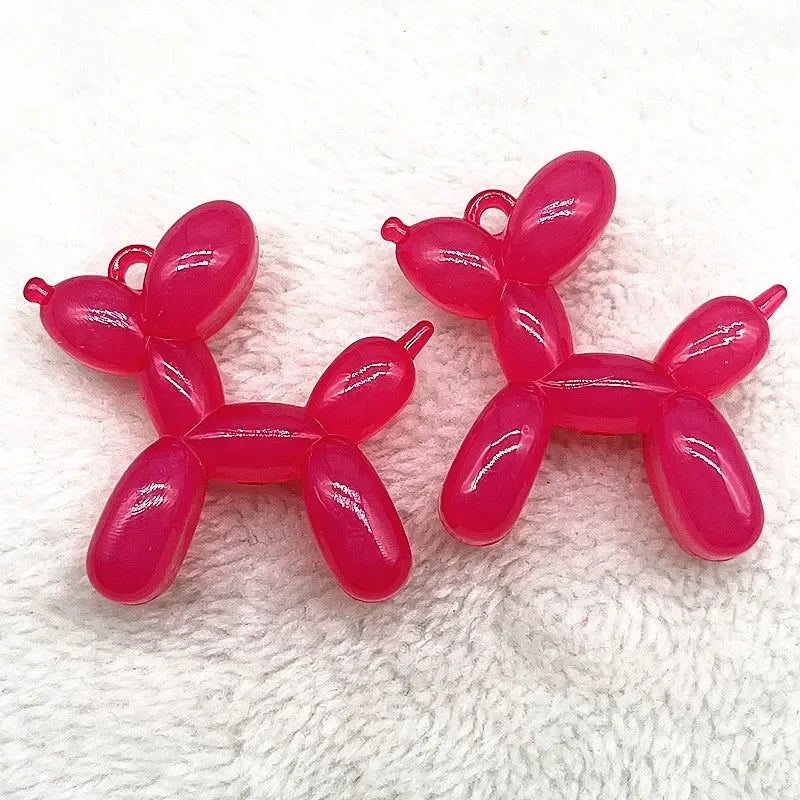 A pair of pink acrylic balloon dog charm pendants displayed on a white, fluffy surface.