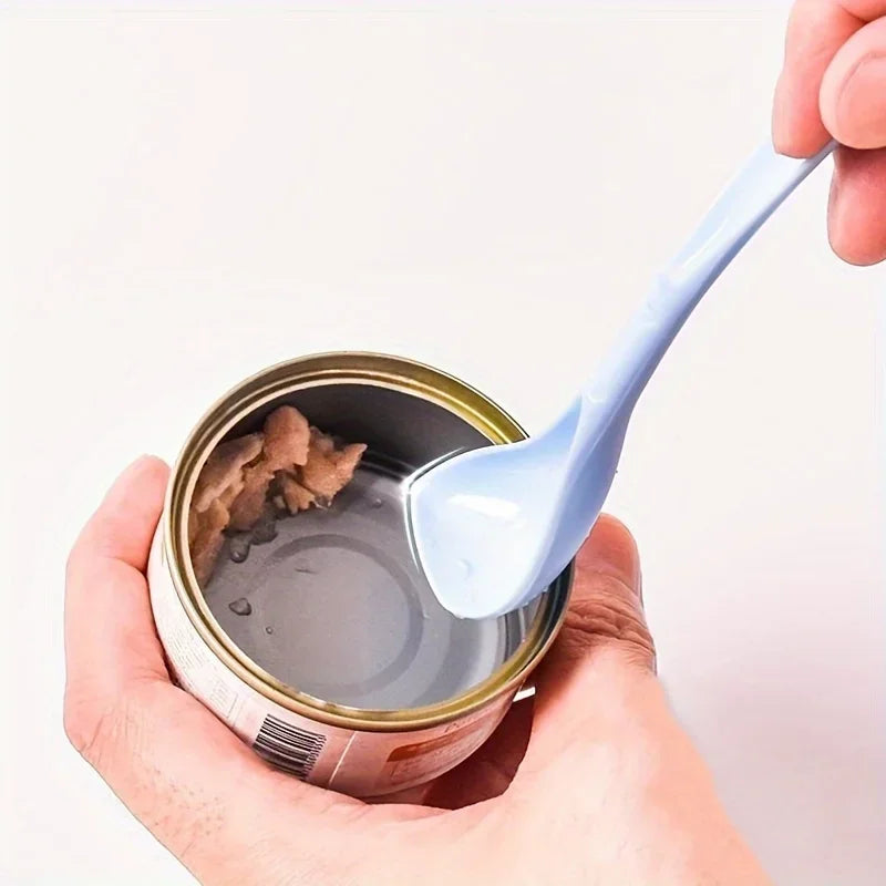 A hand holds an open pet food can with a blue spoon inside.