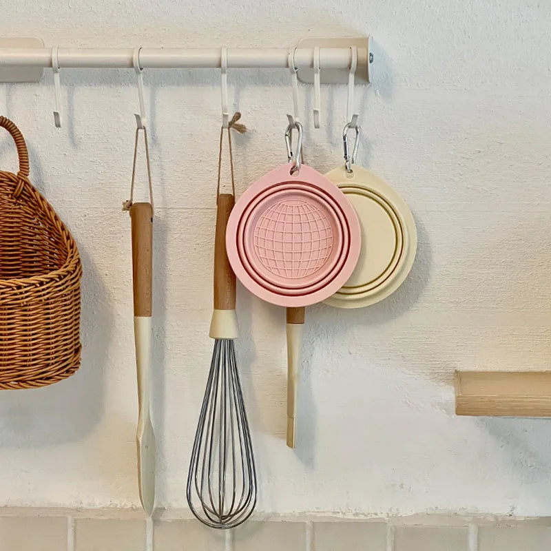 A silicone pet travel bowl hanging on a kitchen rack with various utensils.