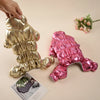 A hand is holding a gold waterproof fleece-lined dog jumpsuit and a pink version of the same garment.