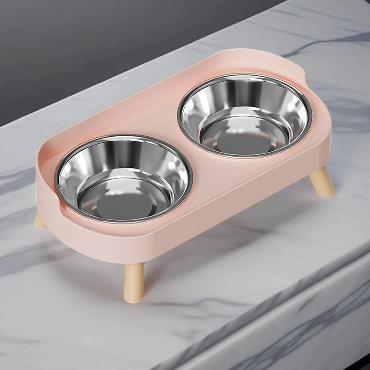 A pink elevated pet feeder with two stainless steel bowls resting on a marble surface.
