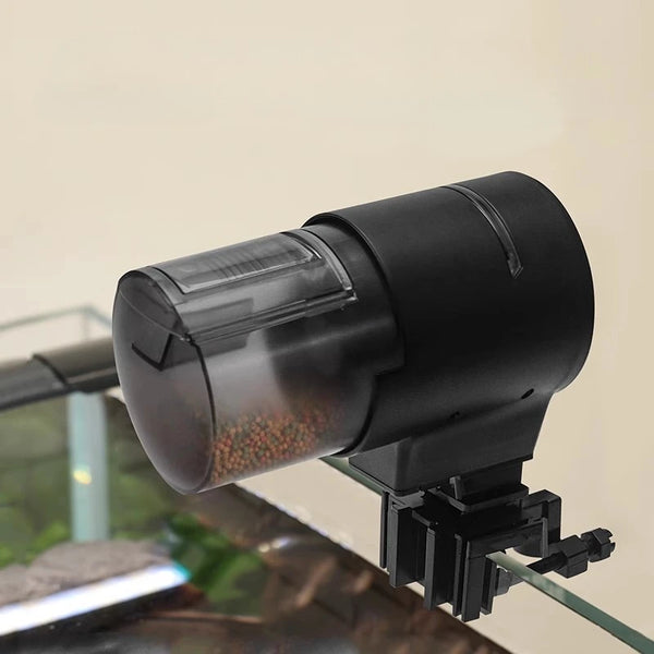 A black smart Wi-Fi automatic fish feeder is shown angled over a dark surface.