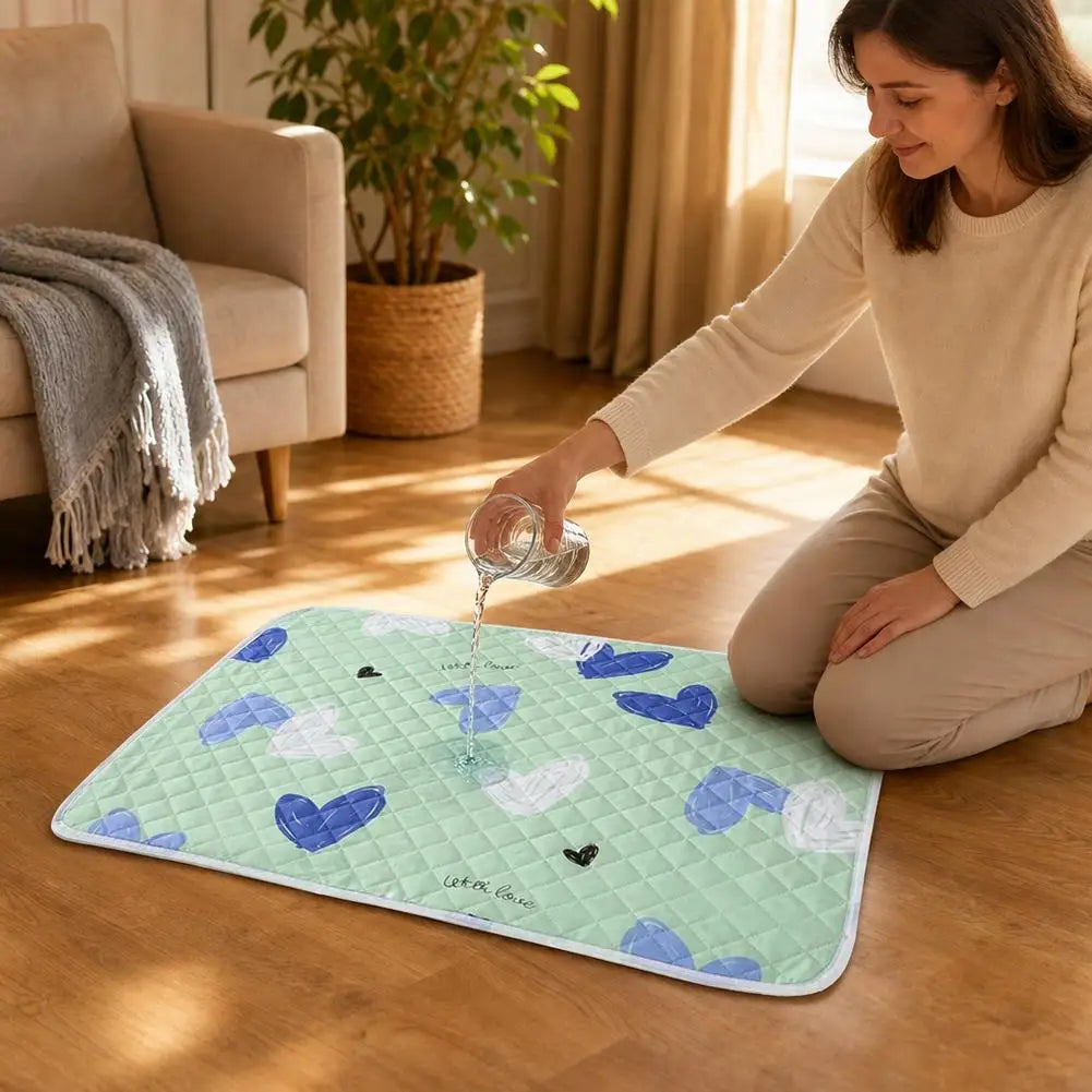 A woman is pouring water onto a light green pet urine pad with blue and white hearts on a wooden floor.