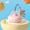 A pink interactive rotating feather cat toy with a transparent dome and a fluffy feather is displayed on a light yellow surfa