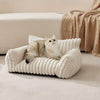 قطة مربعة فروية مسترخية في سرير قطط من المخمل الأبيض والمضلع على أرضية فاتحة اللون.