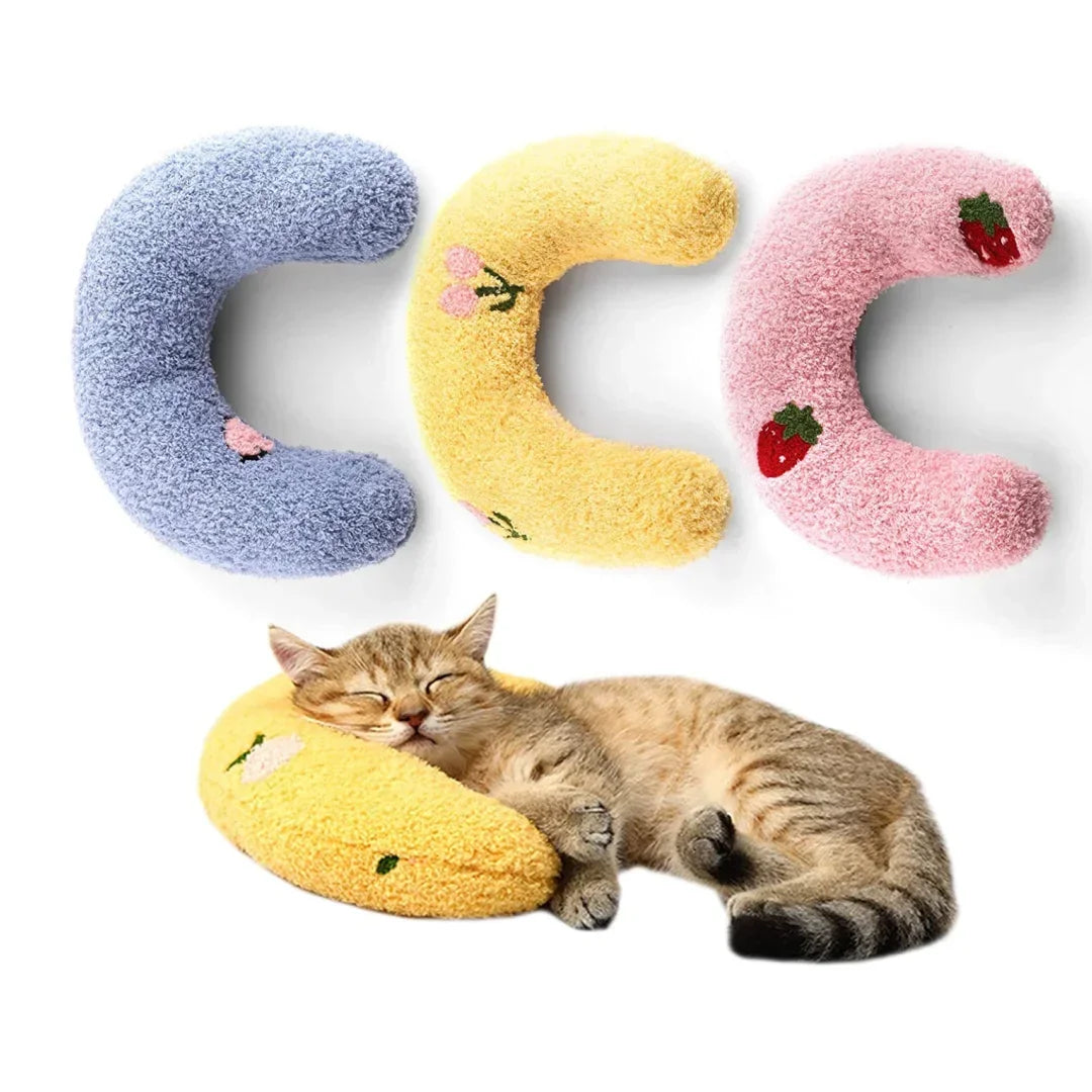 Three U-shaped cat sleeping pillows in blue, yellow, and pink with strawberry designs, next to a tabby kitten.