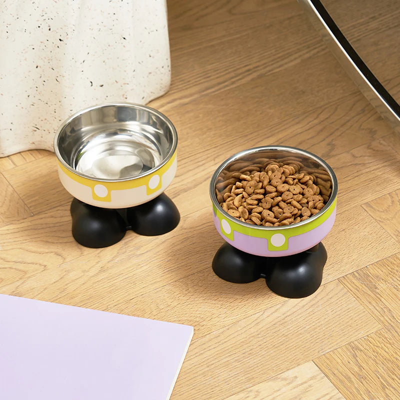 Elevated stainless steel pet bowl with a light yellow rim and black base sitting on a wooden surface.