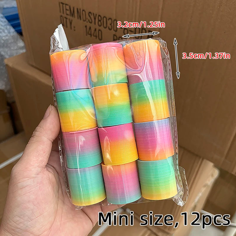 A hand holds a clear plastic package containing 12 colorful rainbow spring coil toys.