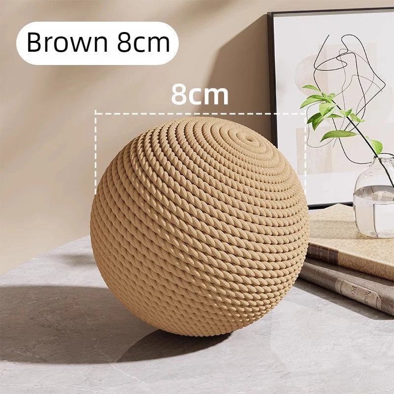 A brown sisal cat toy ball measuring 8cm is shown on a table next to a plant.