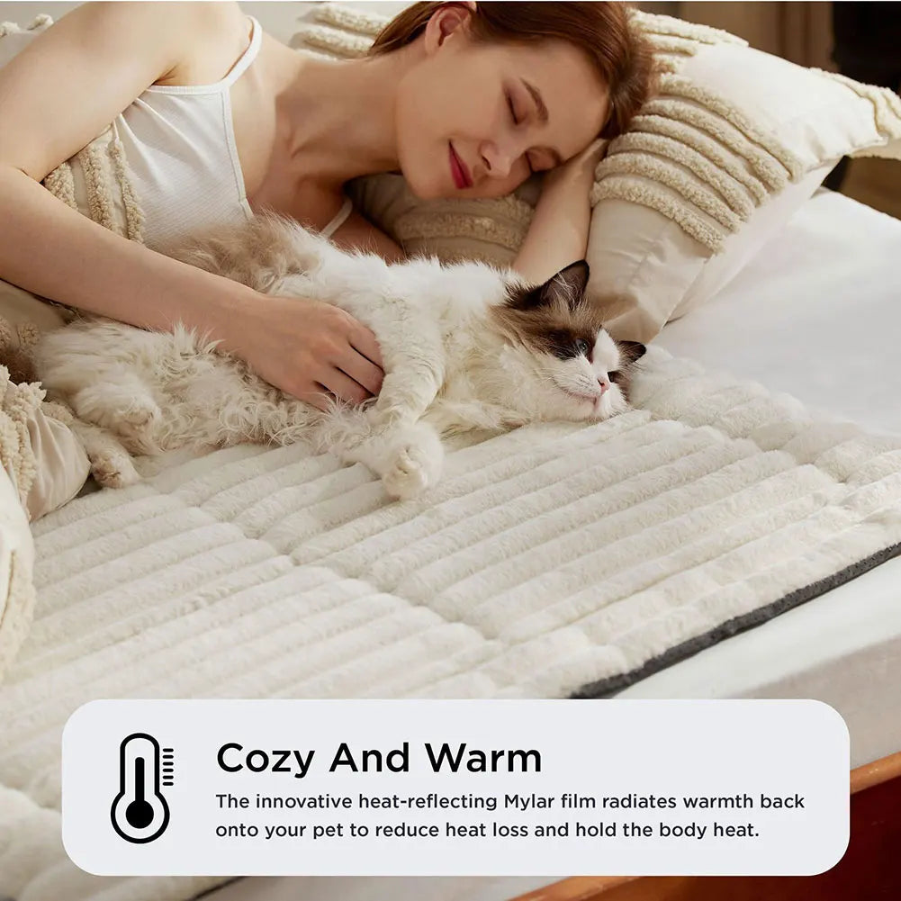 A woman is gently petting a fluffy white cat lying on a thick, quilted pet mat designed to provide warmth.
