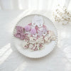Présentation de nœuds élastiques pour cheveux roses et blancs sur une assiette blanche.
