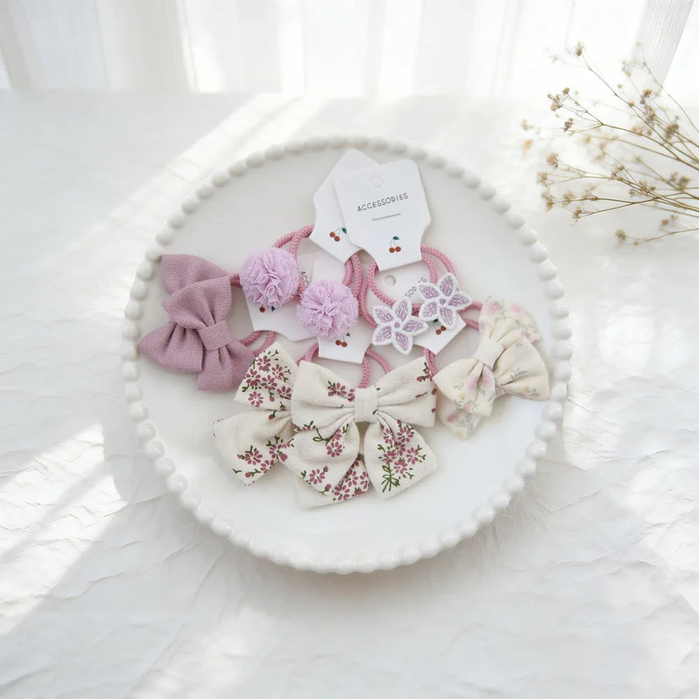 Présentation de nœuds élastiques pour cheveux roses et blancs sur une assiette blanche.